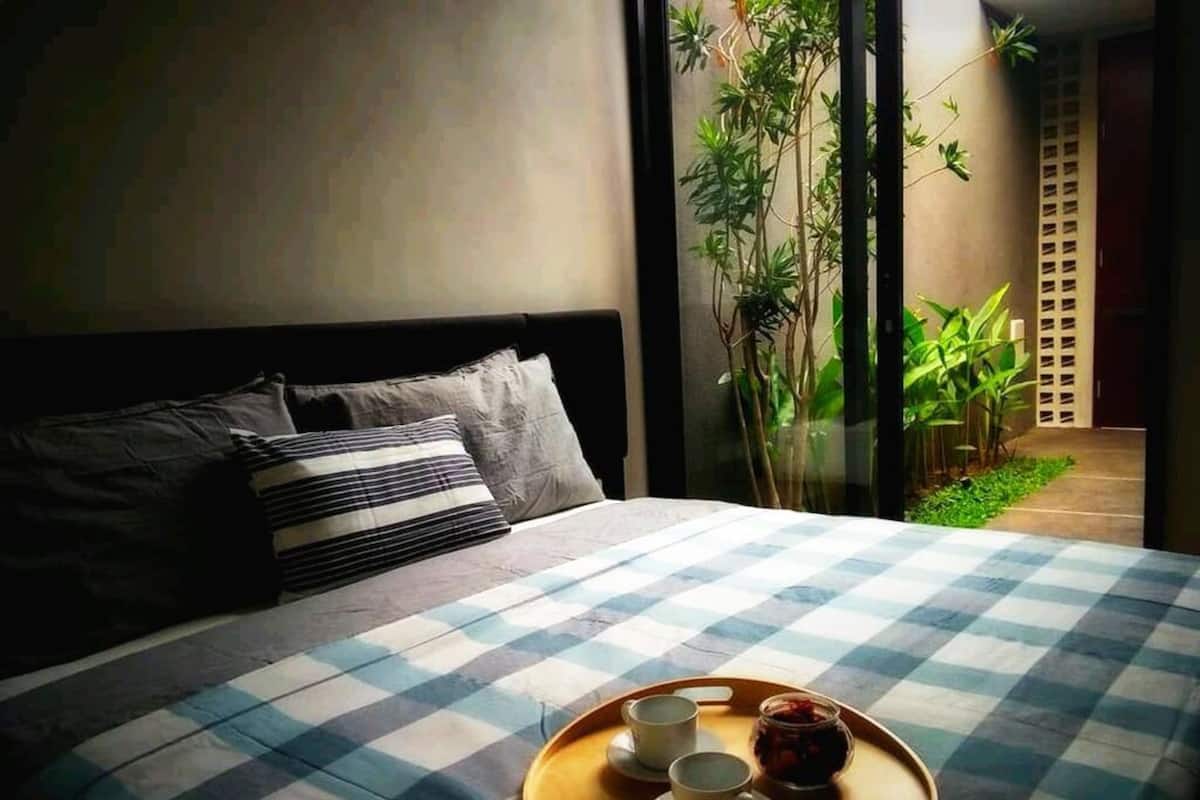 A bed with a checkered bedspread, two cups, and a jar of jam on a tray.