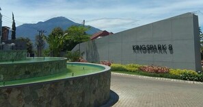 A concrete wall with "KINGSPARK 8" written on it, a landscaped area with a fountain, and mountains in the background. - Group Villa Luxury (Batu)