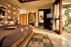 A bedroom with a large bed, a wooden wardrobe, a mirror, and a television. - Villa Brabhan Seminyak (Seminyak)