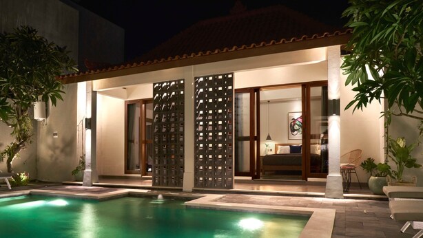 Área da piscina com piscina transparente, espaço coberto para sentar e vista para um quarto.