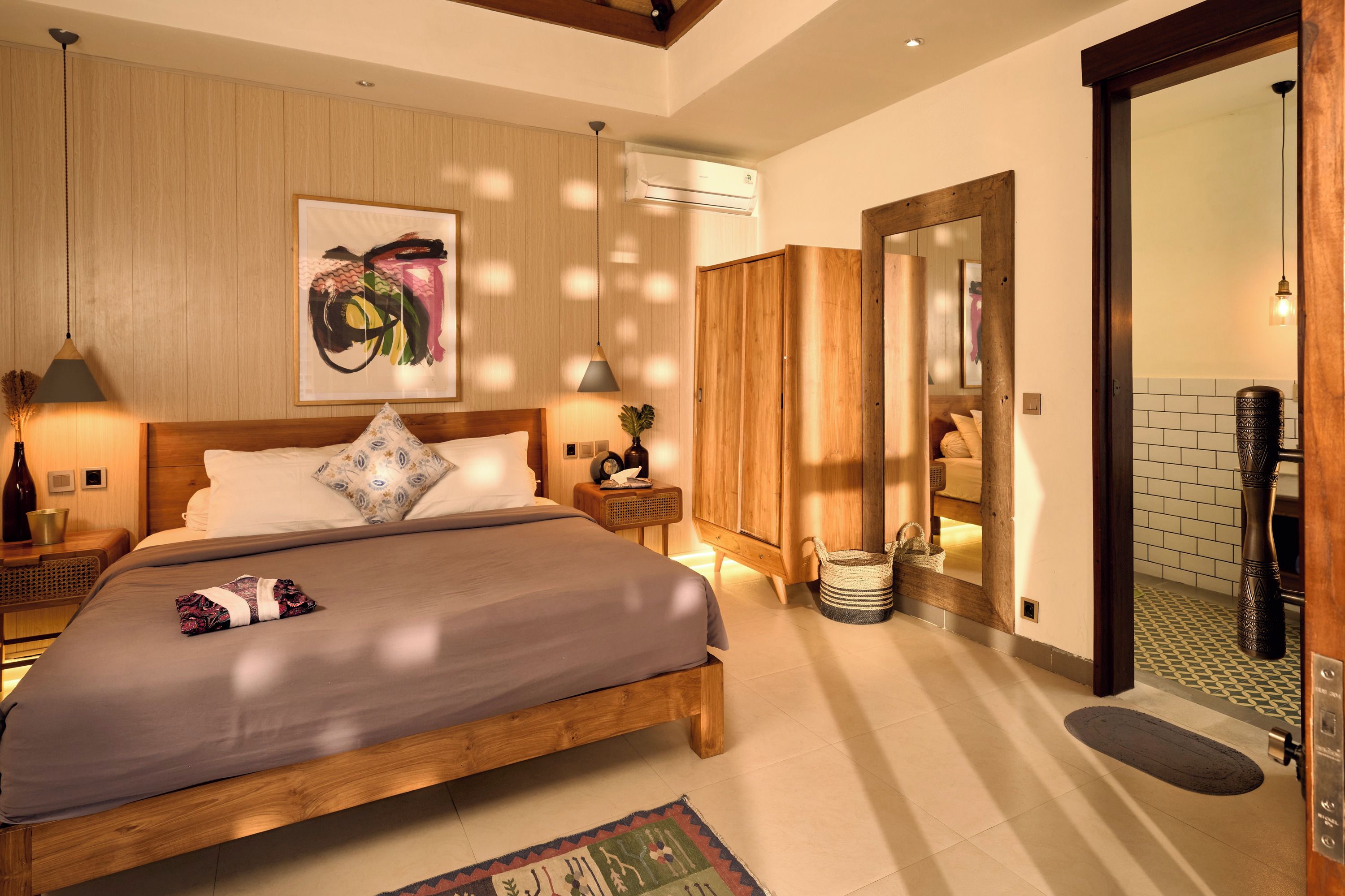 A bedroom with a wooden bed, a large painting, a wardrobe, and a bathroom visible through an open door.