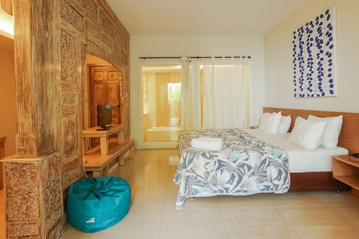 A bedroom with a bed, a wooden headboard, a blue bean bag, a TV, and a decorative wall piece.