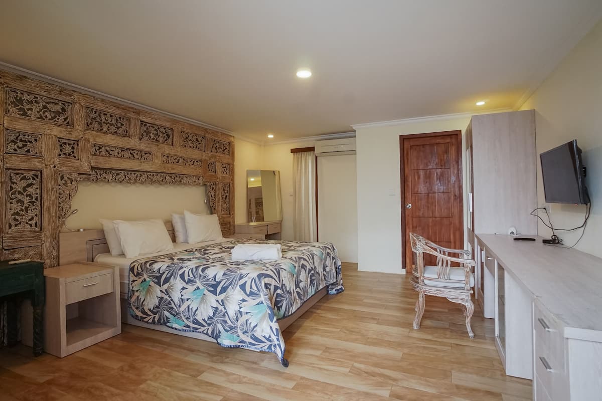 A bedroom with a bed, wooden headboard, nightstand, dresser, chair, and a TV.