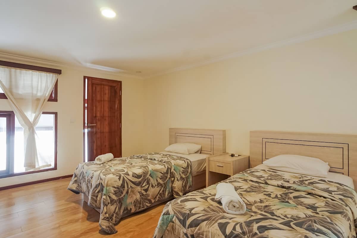 A room with two beds, wooden flooring, a window with curtains, and a door.