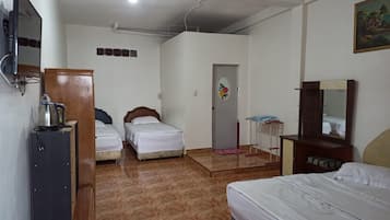 A hotel room with two single beds, a wooden wardrobe, a desk with a kettle, a mirror, and a door with a floral decoration.
