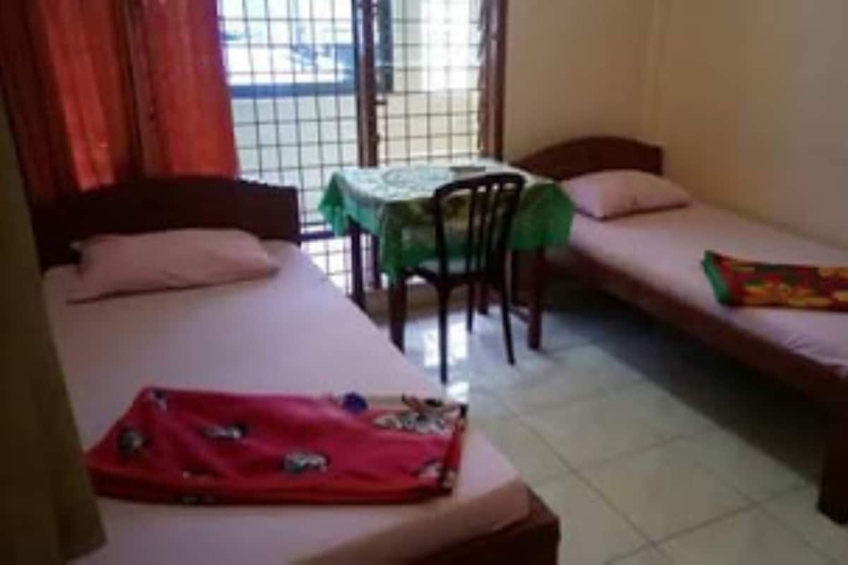 A room with two single beds, a small table with a green tablecloth, and a chair.