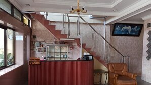 A reception area with a red counter, a staircase, a leather armchair, and a wall-mounted TV.