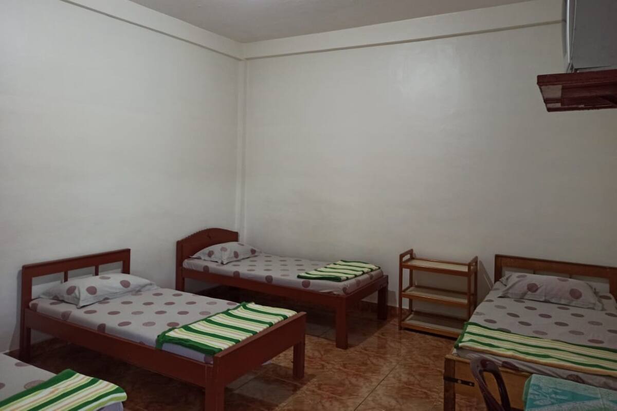 A small, clean room with three wooden beds, each with a polka dot and striped bedspread.