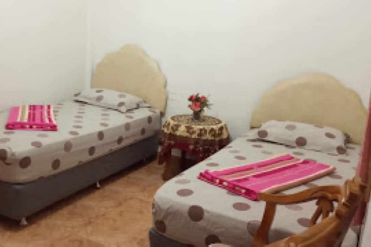 A bedroom with two single beds, each with a polka dot bedspread and a pink blanket. There is a small round table with a vase of flowers between the beds.