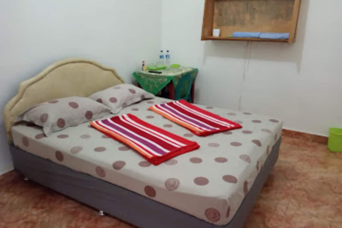 A bed with a polka dot bedspread and striped pillows, a small table with a green tablecloth, and a green trash bin.