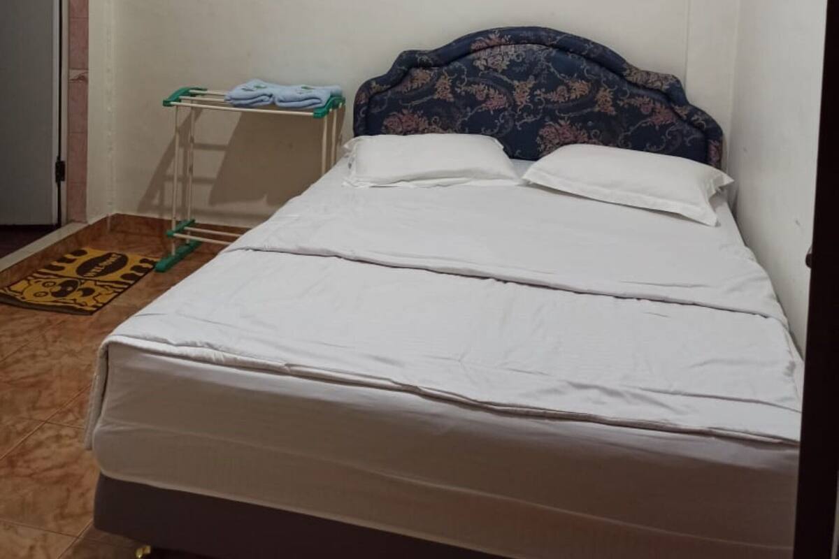 A simple, clean room with a bed, a small table with a towel, and an air conditioning unit.