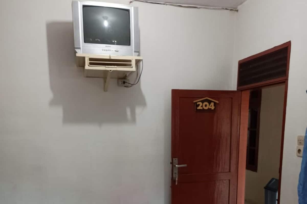 A small, simple room with a bed, a television mounted on the wall, and a door with the number 204.