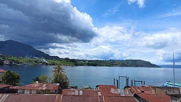 A coastal view with a mountain in the background, a body of water, and a building with a rusted roof.