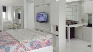 A bedroom with a bed, a TV mounted on the wall, a wardrobe, and a small kitchenette area. - Apartment Gading Nias Residence (Jakarta)