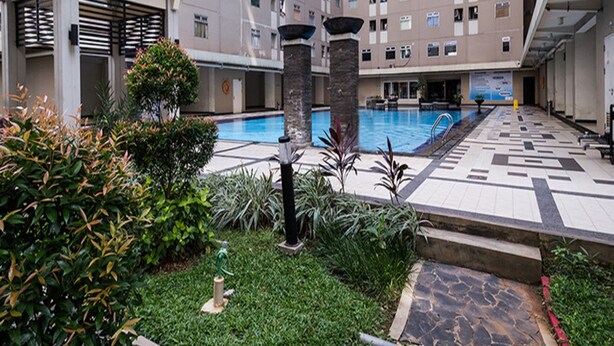 An indoor swimming pool with a tiled floor, surrounded by greenery and a multi-story building with balconies. - Apartment Gading Nias Residence (Jakarta)