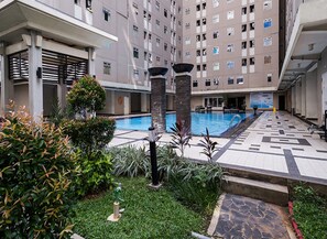 An indoor swimming pool with a tiled floor, surrounded by greenery and a multi-story building with balconies. - Apartment Gading Nias Residence (Jakarta)