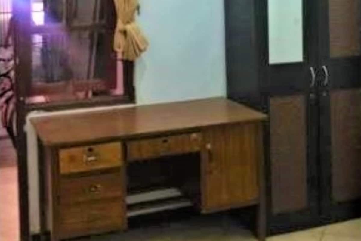 Een houten bureau met lades en een plank, staand in een kamer met een betegelde vloer en een deur op de achtergrond.