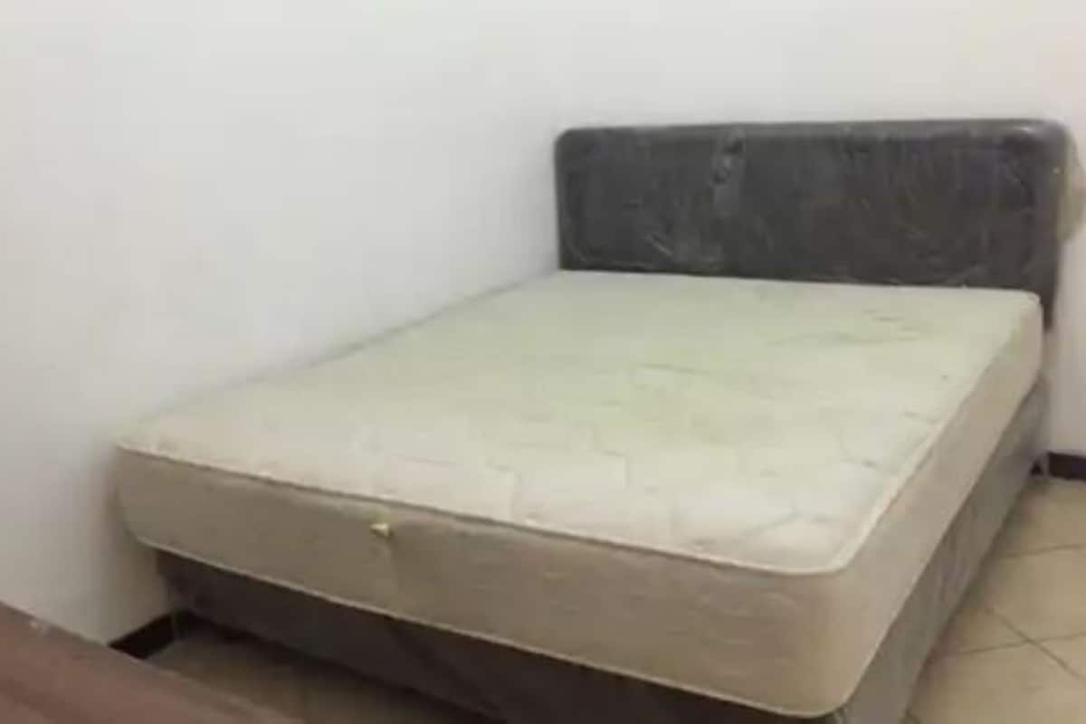 Een kleine eenpersoonskamer met een simpel matras en een eenvoudig hoofdbord.