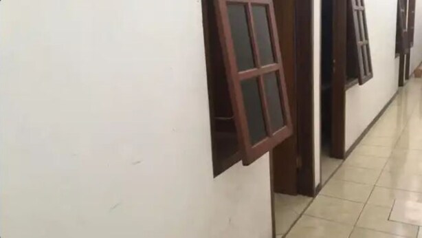 A corridor with a white wall and a door with a window. - Penginapan Meli (Surabaya)