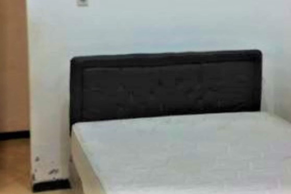 A single bed with a dark headboard in a room with plain white walls.