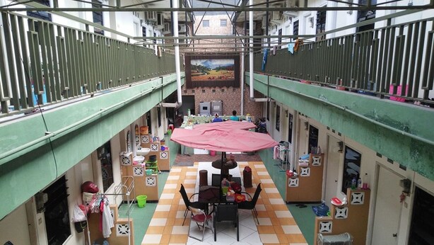 Une cour intérieure avec une table et des chaises au centre, entourée de divers objets et ornée d’une fresque murale.