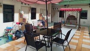 Un coin repas avec une table et des chaises, un parasol rose et un distributeur d’eau.