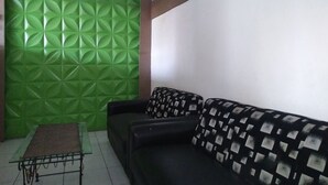Une pièce avec un mur vert à texture, un canapé noir orné de coussins à motifs et une petite table sur laquelle est posé un tapis marron.