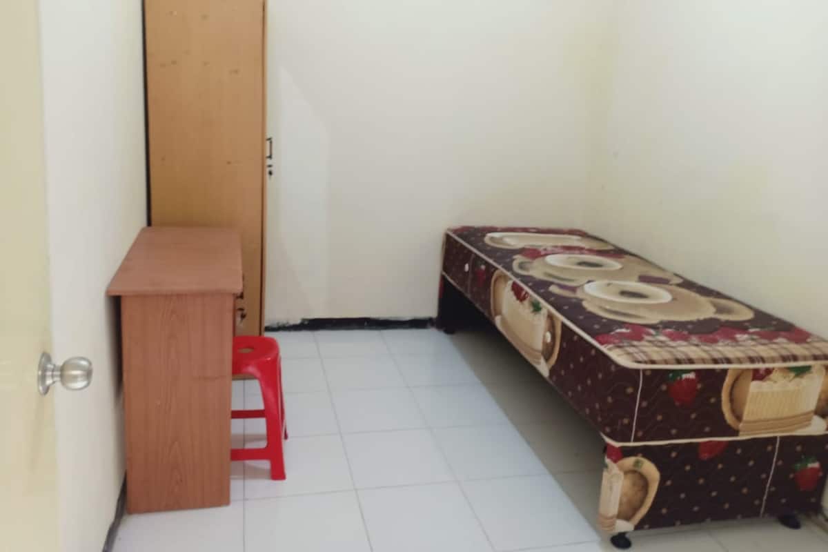 A small room with a wooden desk, a red stool, and a bench with a fruit pattern.