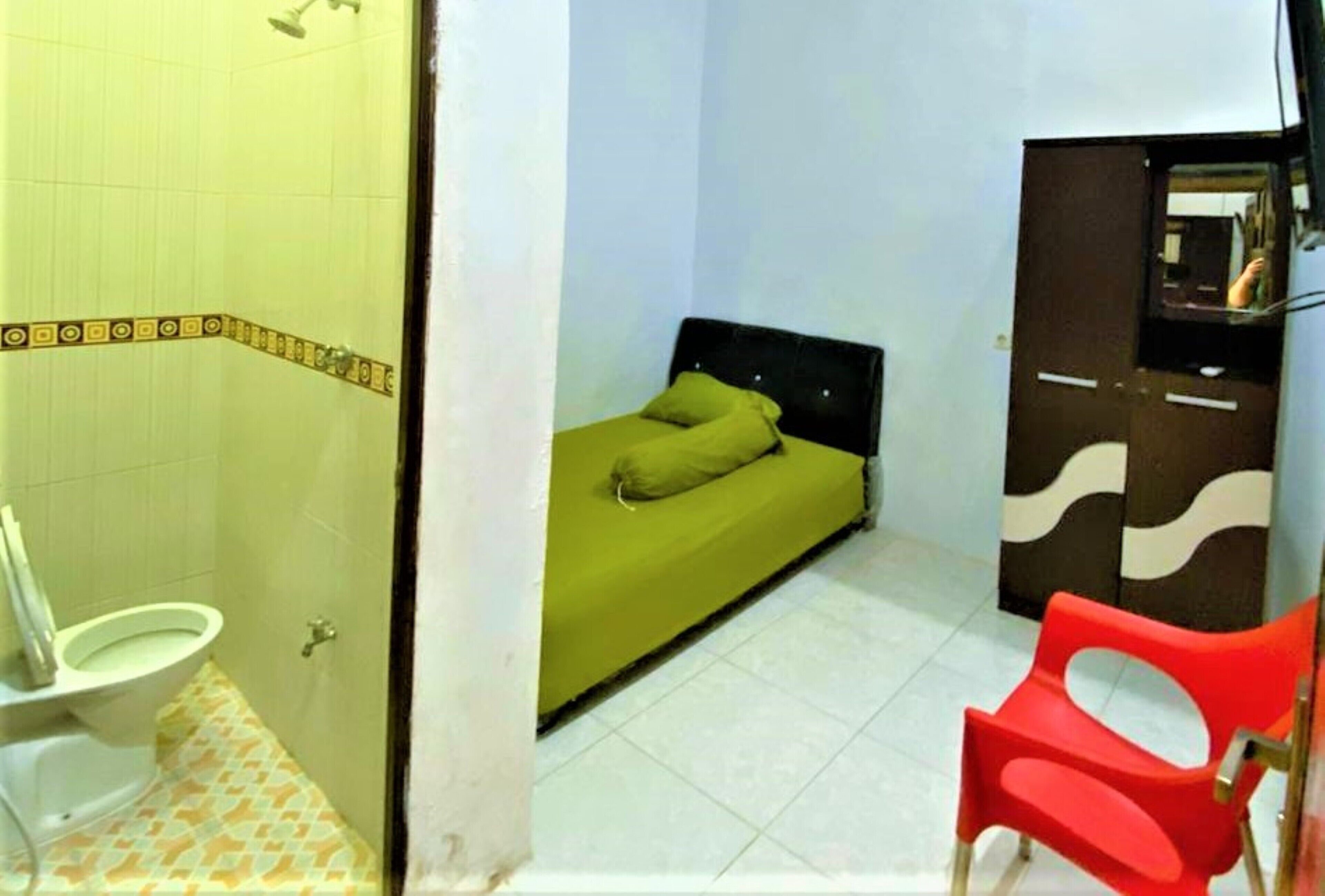 A small room with a bed, a chair, a wardrobe, and a toilet.