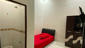 A small, compact room with a bed, a shower, a toilet, and a wardrobe. - Radja Guest House (Makassar)
