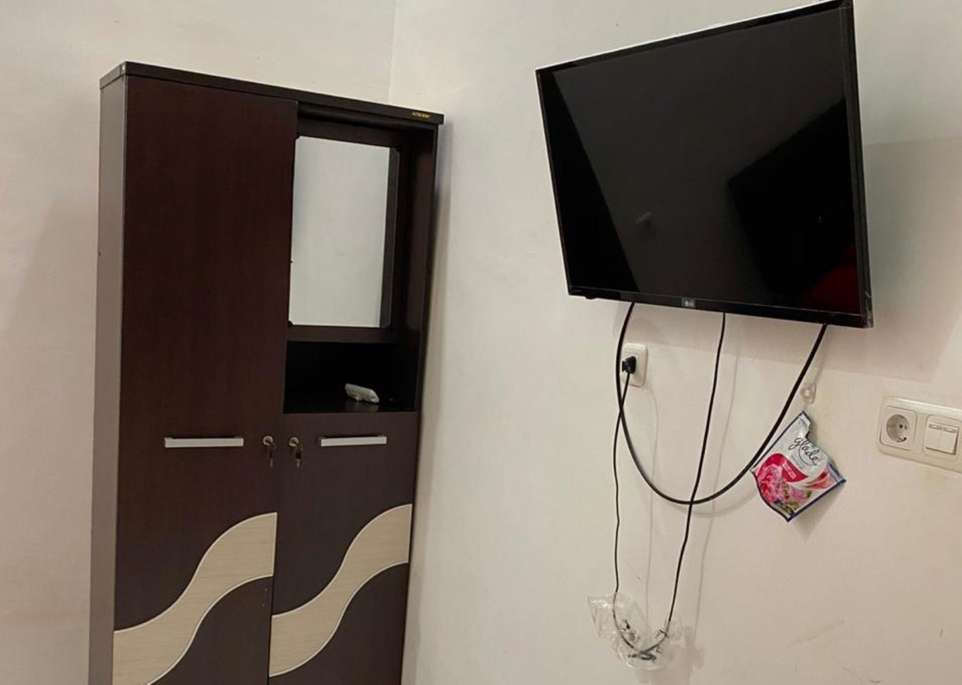 A room with a wardrobe, a flat-screen TV mounted on the wall, and a power outlet with a cable.