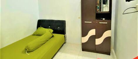 A single bed with green bedding and pillows, a wardrobe with a mirror, and a red chair.