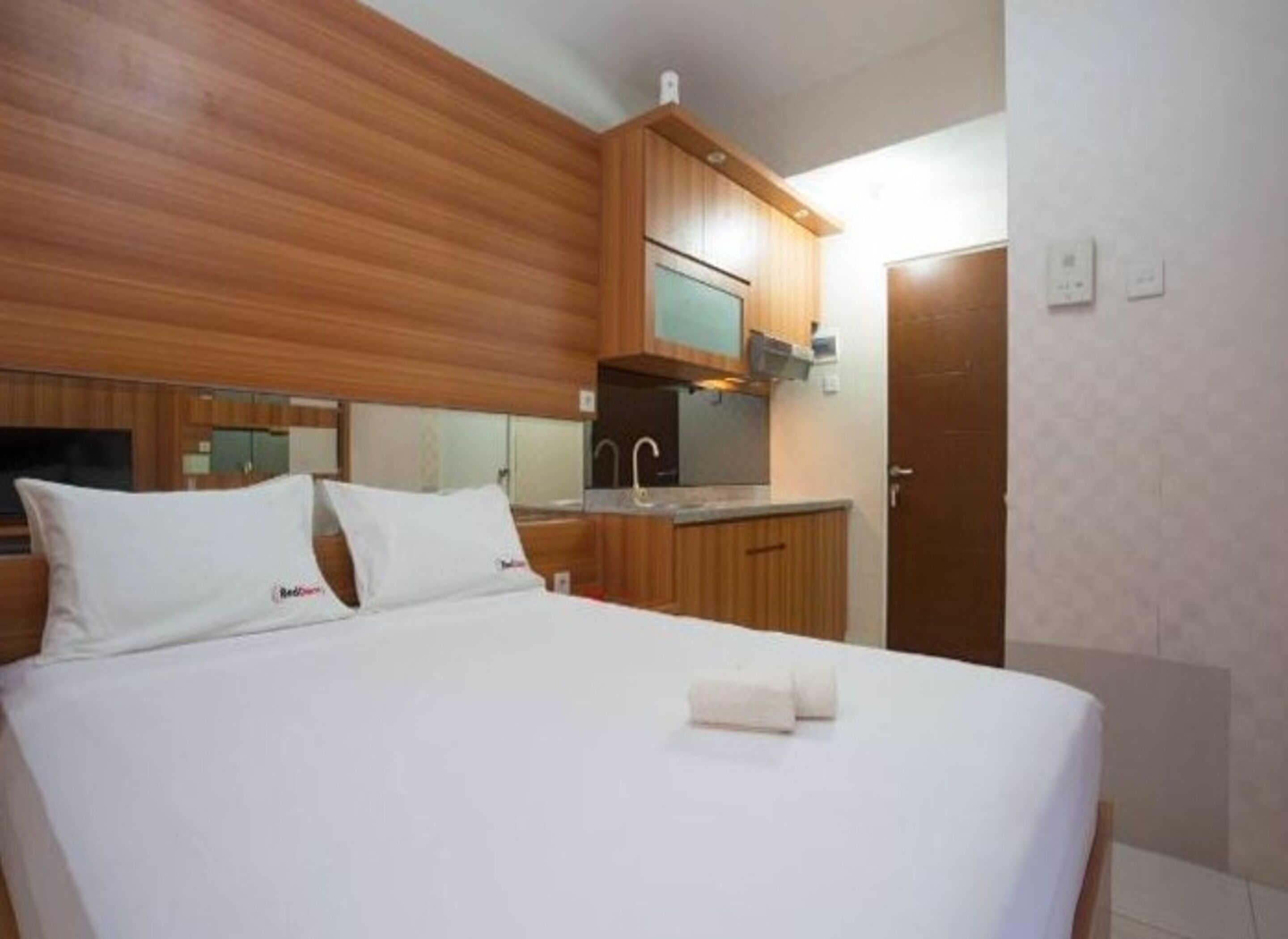 A hotel room with a bed, a small kitchenette, and a door.