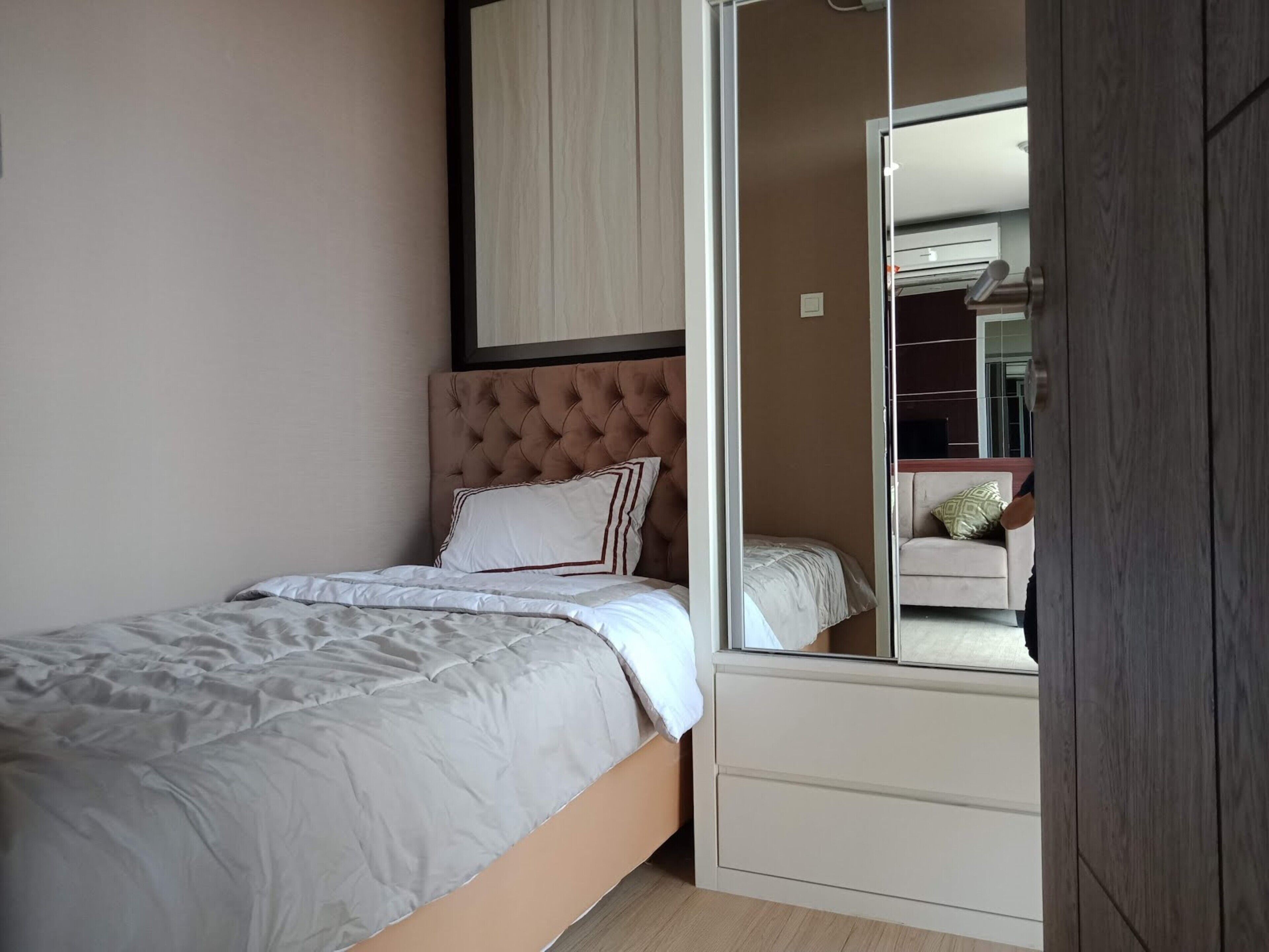 Une chambre à coucher avec un lit, une armoire et un miroir qui reflète un canapé et une lampe.