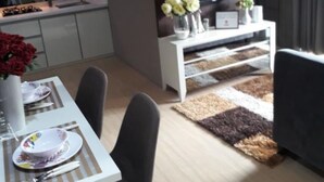 A modern living room with a flat-screen TV, a dining table set with plates and a vase of flowers, and a sofa. - Apartment Taman Melati Surabaya by Havana Friends (Surabaya)