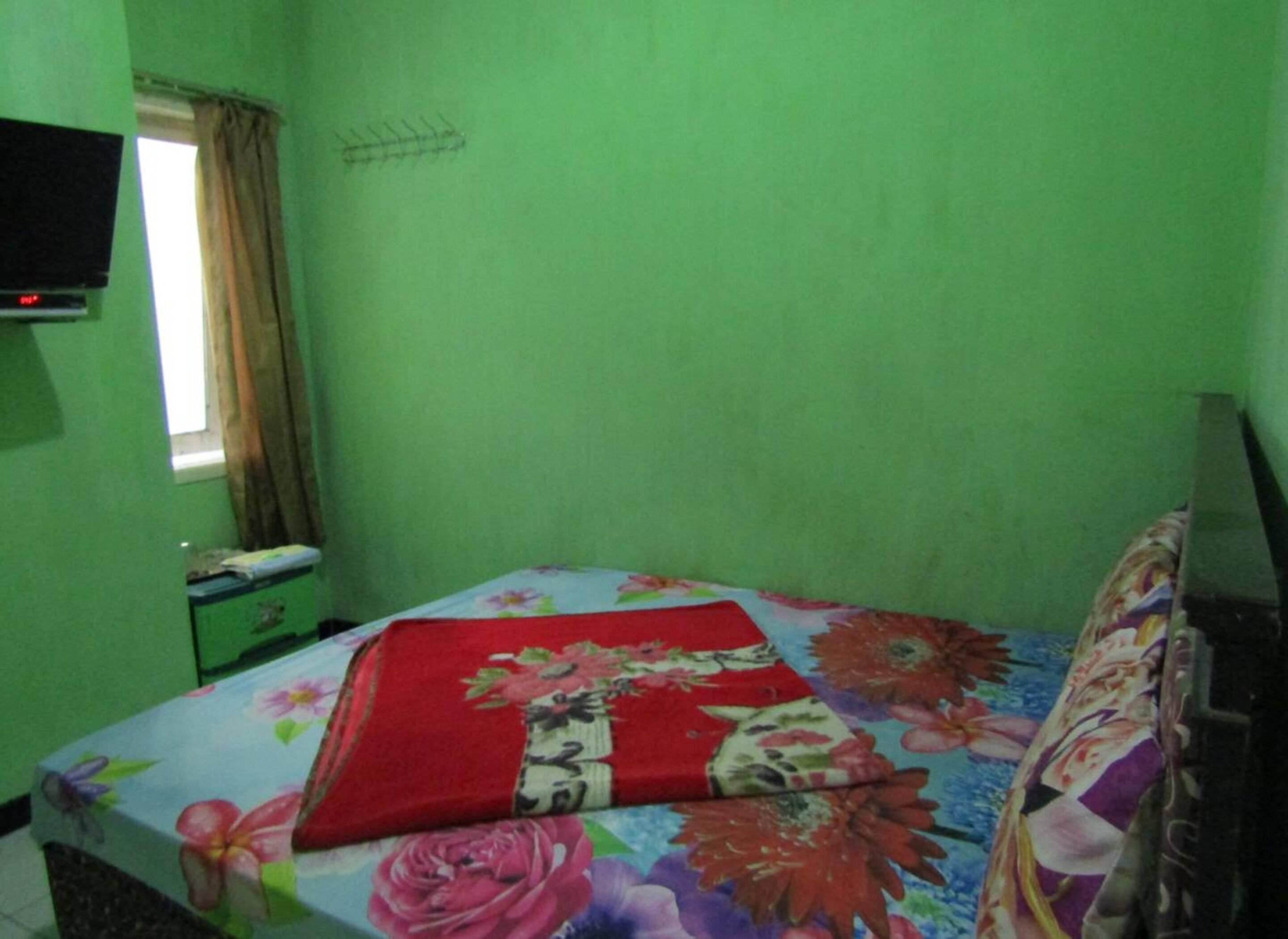 A small, green-walled room with a bed, a television, and a window with curtains.