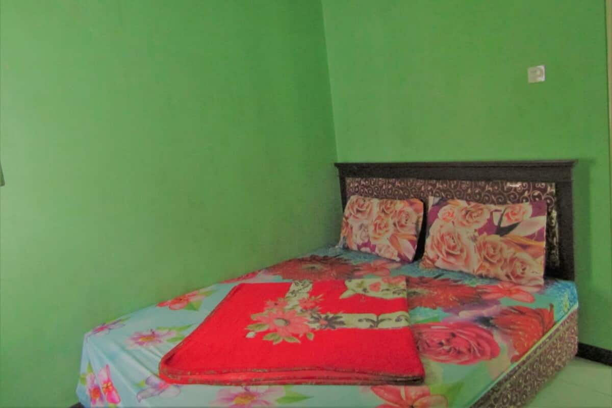 A single bed with floral bedding and a red throw blanket in a room with green walls.