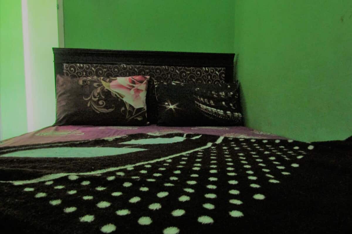 A bed with a polka dot blanket, two pillows with floral and star patterns, and a green wall.