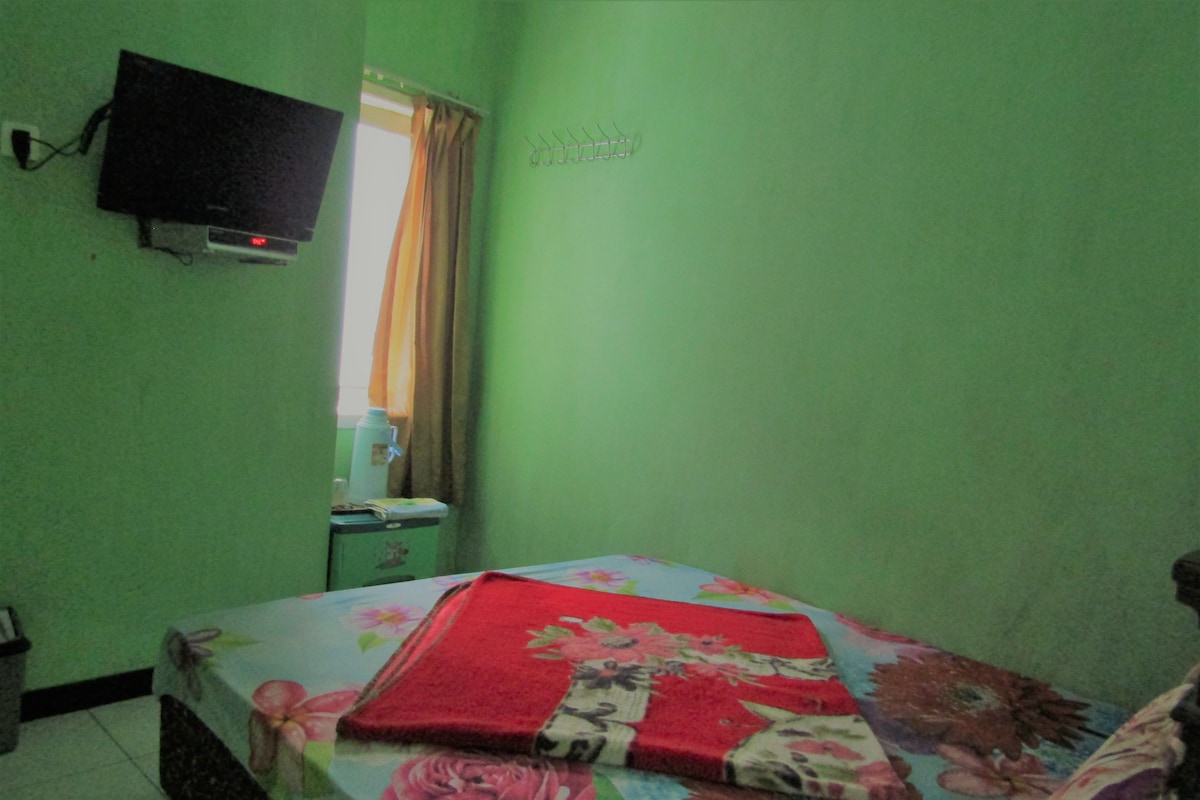 Quarto com uma cama, televisão fixada na parede e janela com cortinas.