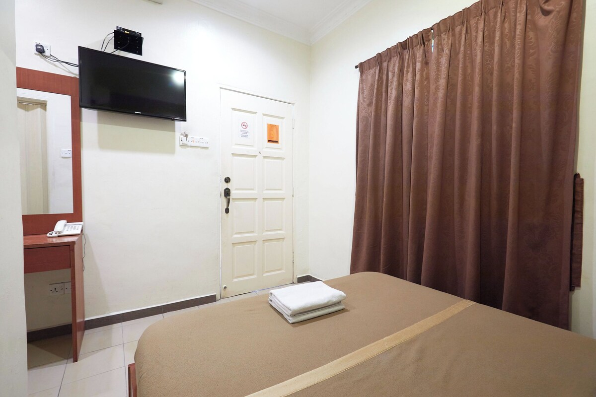 Habitación de hotel con una cama, un escritorio con teléfono, un televisor en la pared y una puerta con un cartel.