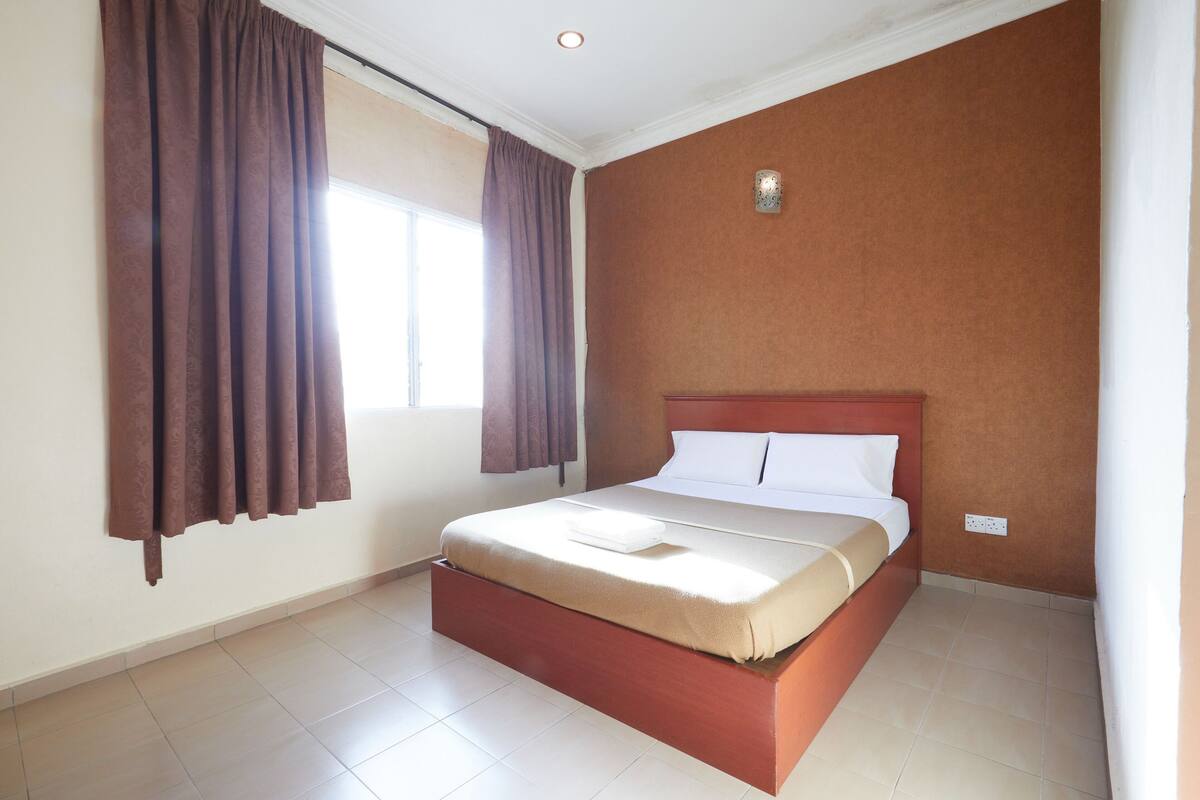 A hotel room with a bed, curtains, a window, and a wall socket.
