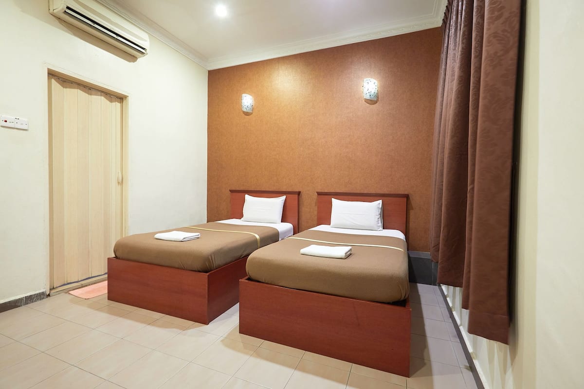 A hotel room with two beds, a wooden door, an air conditioner, and a curtain.
