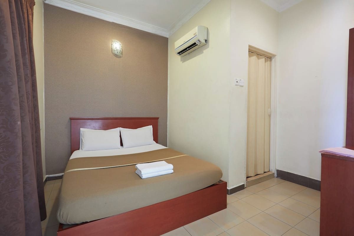 A hotel room with a single bed, a wooden headboard, a white air conditioner, and a door with a wooden frame.