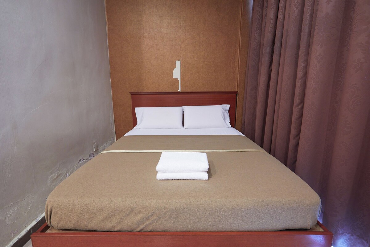 A neatly made bed with a brown bedspread and white pillows, a wooden headboard, and a brown curtain on the right.