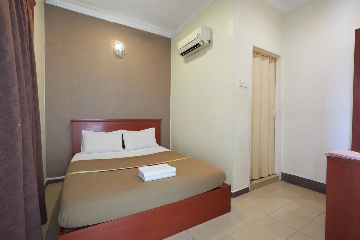 A hotel room with a single bed, a wooden headboard, a white air conditioner, and a door with a wooden frame.