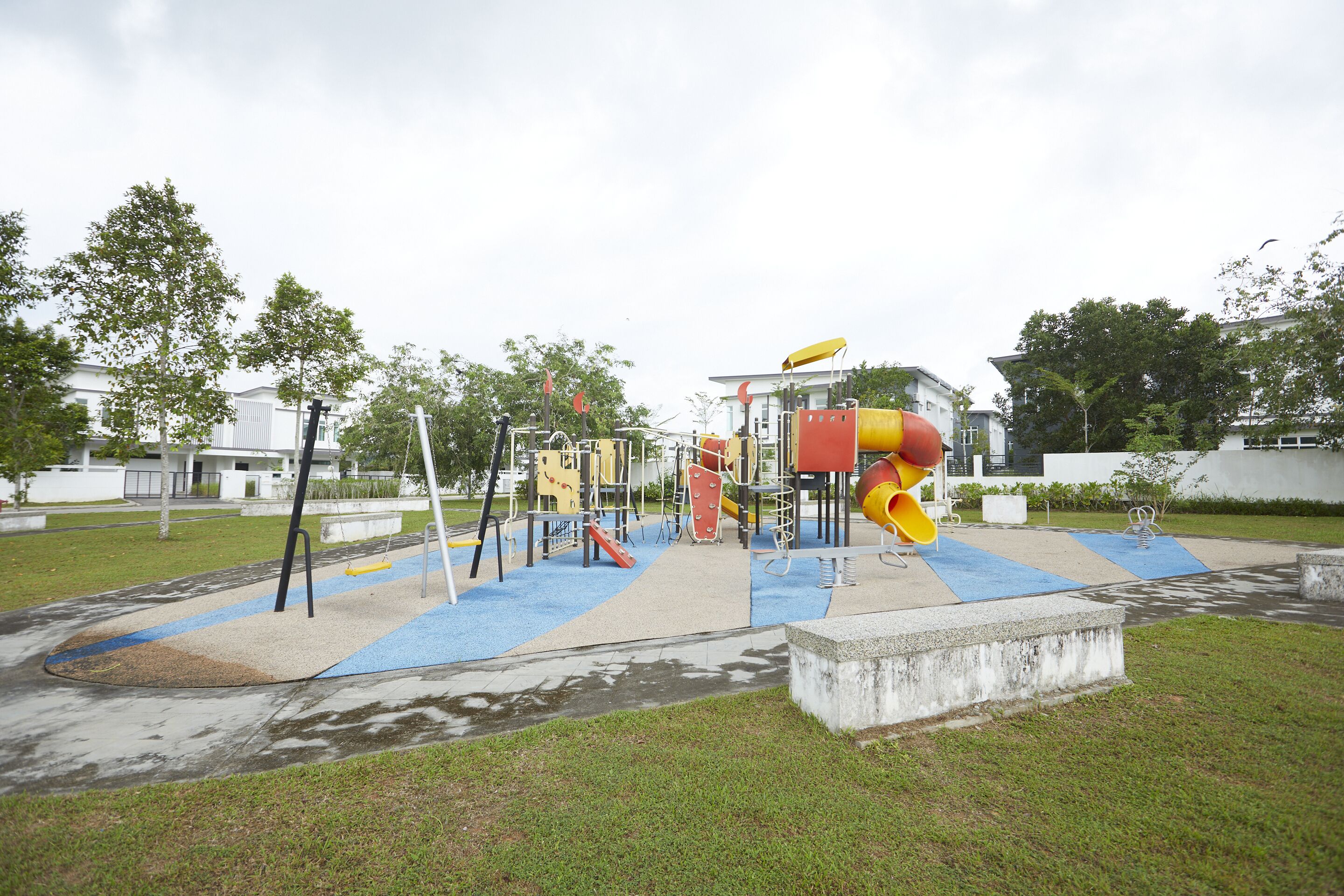 Un parc infantil amb diverses estructures de jocs, incloses tobogans i cadenes, envoltat d'herba i arbres.