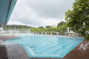 Ein rechteckiger Pool mit Holzterrasse, umgeben von einem Zaun und Palmen.