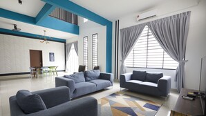 A modern living room with two grey sofas, a patterned rug, and a large window with curtains. - Desaru Arcadia Villa By Convergence (Bandar Penawar)