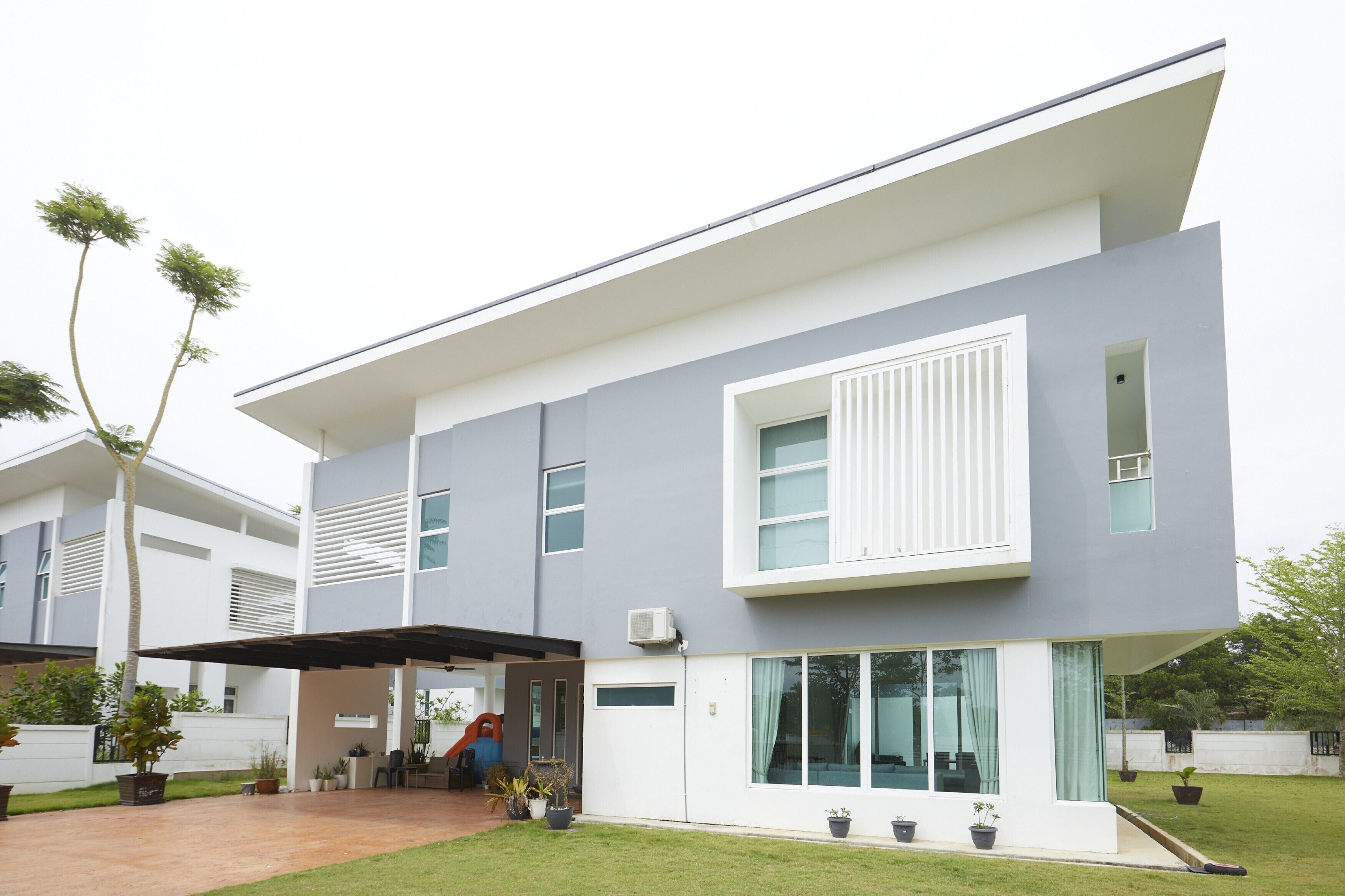 Una casa moderna de dos pisos con techo plano, ventanas amplias y un patio cubierto.