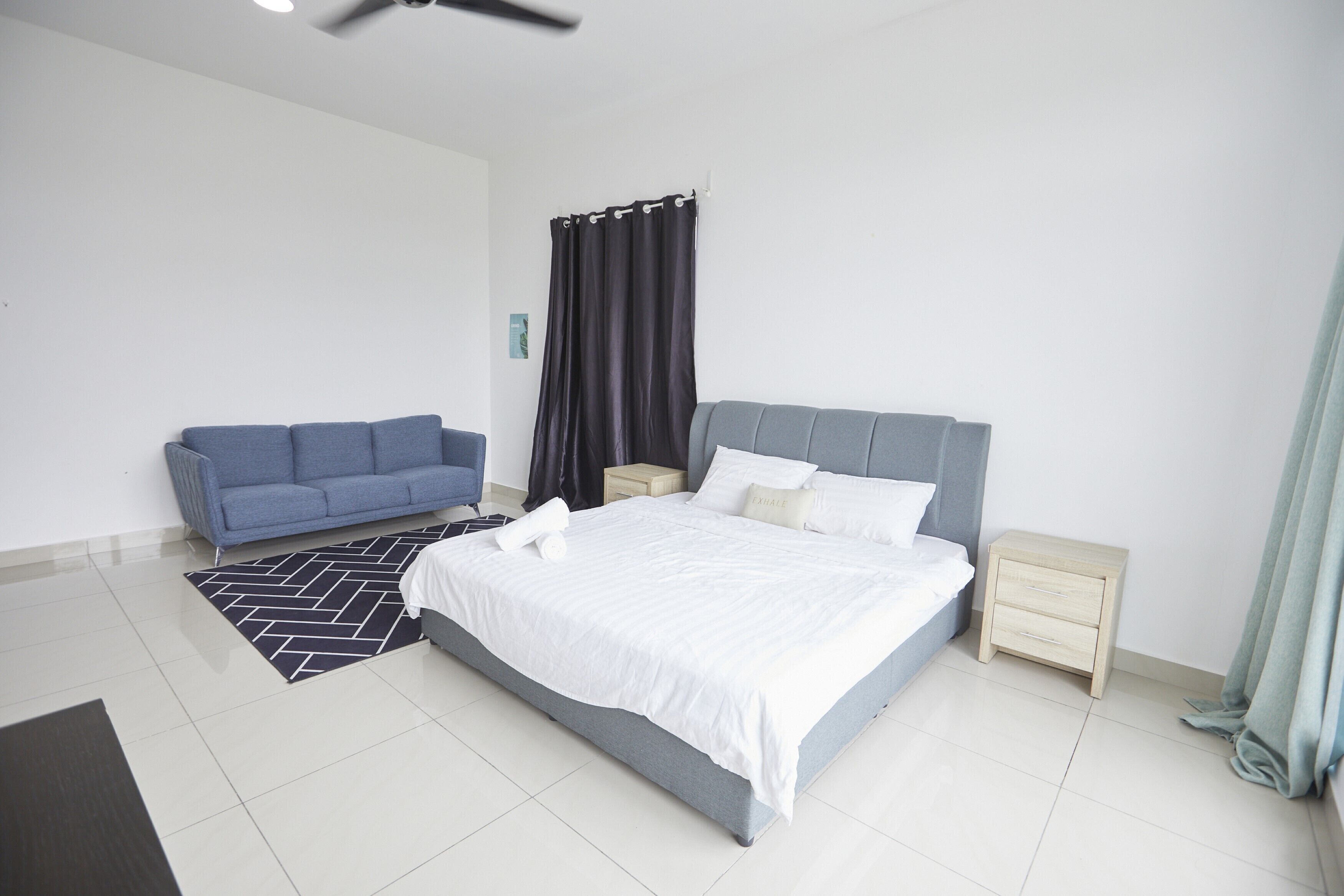 Un dormitorio moderno con una cama grande, un sofá azul, una mesita de noche pequeña y una mesita auxiliar.